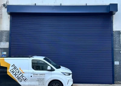 Blue industrial roller shutter door installed by Prestige Doors with company van on site